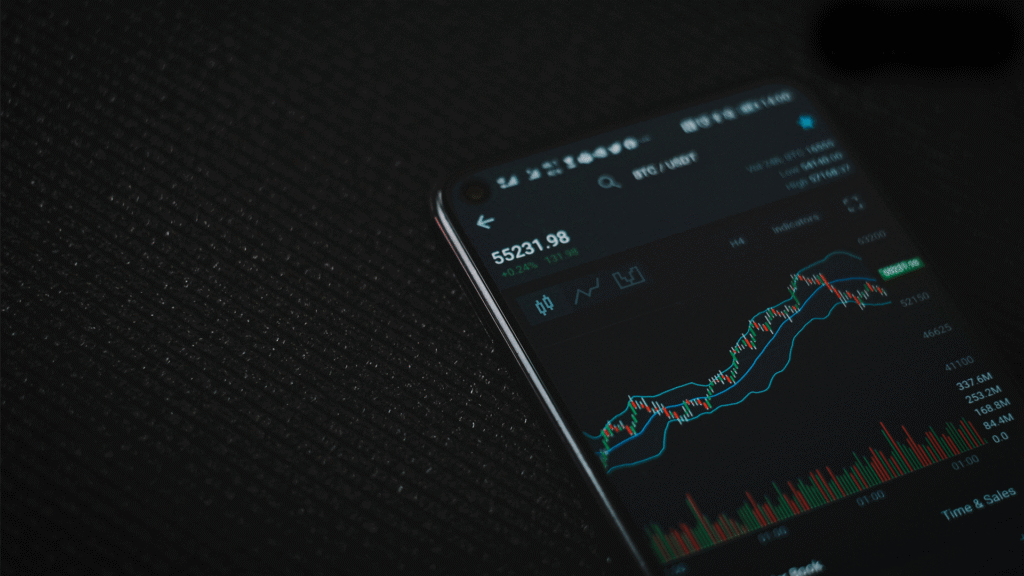 A close-up of a smartphone screen displaying various financial stock graphs and charts, representing the digital tools used for passive or active investing on the go.