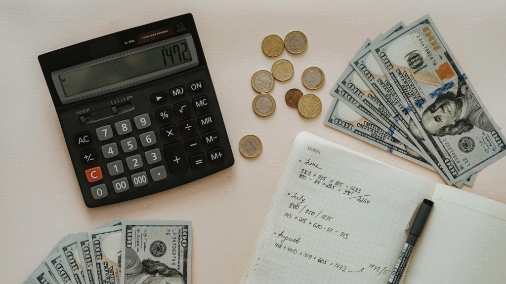 Calculator, euro coins, US hundred dollar bills, and a notebook with financial notes, illustrating how interest rates impact personal budgeting and investment planning.