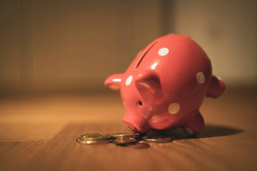 A classic pink piggy bank sits on the floor with a few coins around it, symbolizing the initial savings that grow into larger investments.