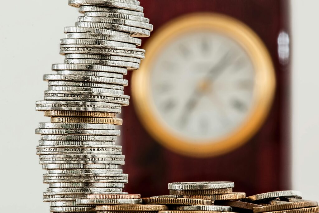 A tall, leaning stack of coins with a blurred clock in the background, symbolizing the effect of interest rates on investment strategies.