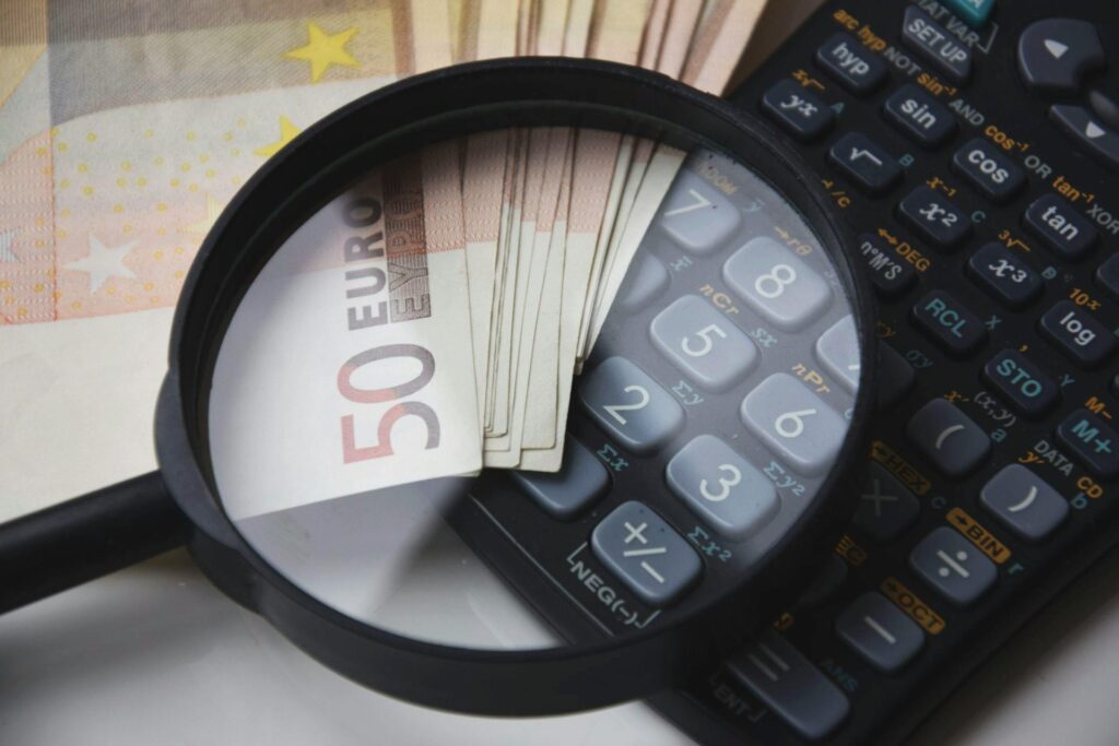 A magnifying glass focusing on 50 Euro banknotes placed near a calculator, symbolizing financial scrutiny and the impact of inflation.