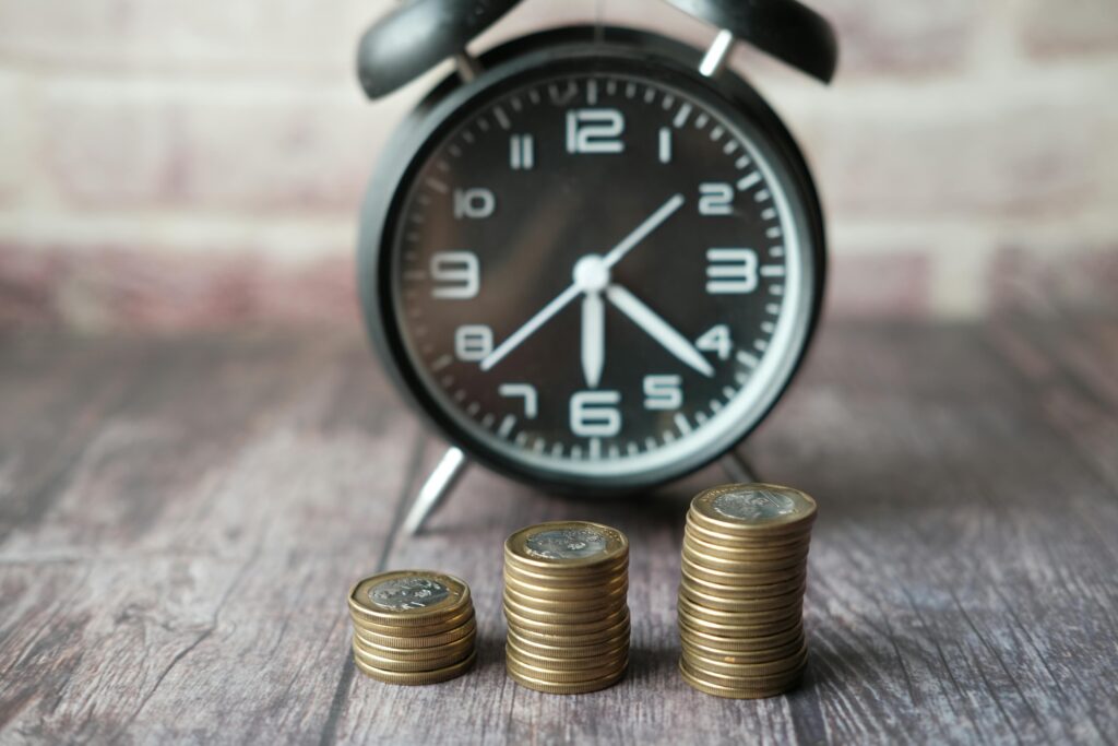 A black alarm clock with stacks of coins increasing in height, symbolizing the impact of time and interest rates on financial growth.