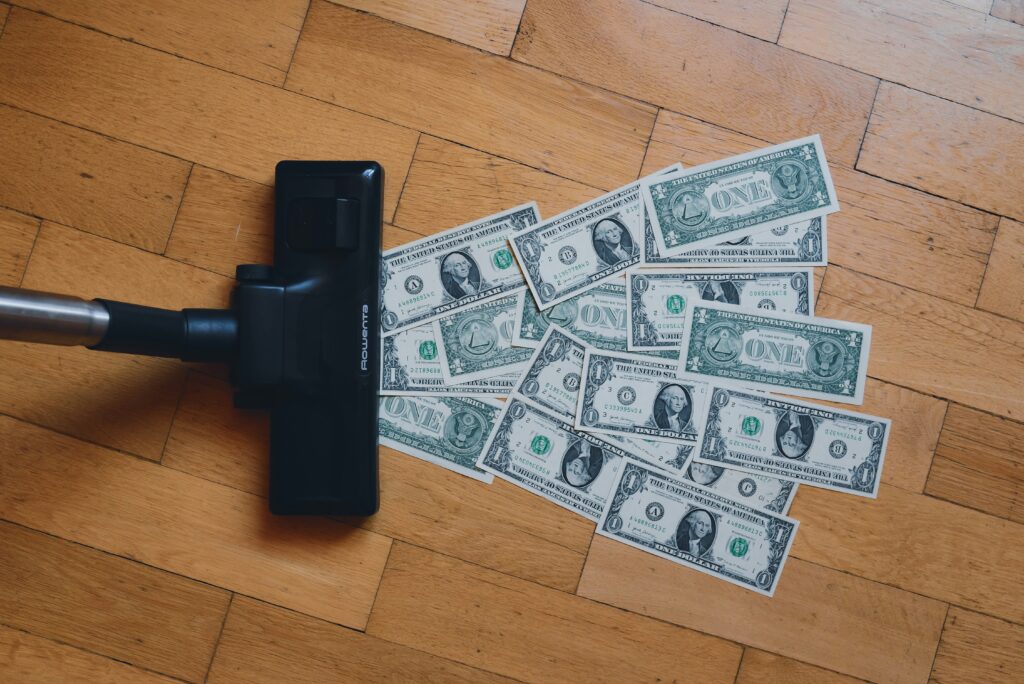 A vacuum cleaner sucking up multiple U.S. dollar bills on a wooden floor, symbolizing the erosion of money's value.