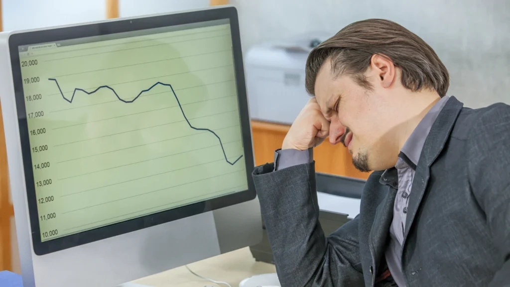 Person looking disappointed at a computer screen showing financial traps with a downward trending graph.