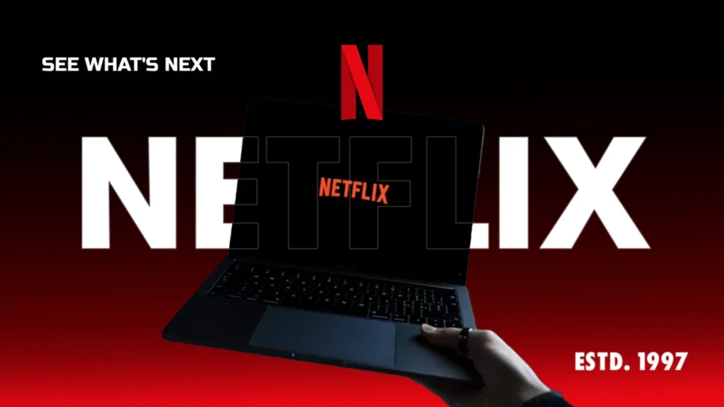 A hand holding a laptop with the Netflix logo on screen, set against a bold red and black background with the text “See What’s Next” and “ESTD. 1997.”
