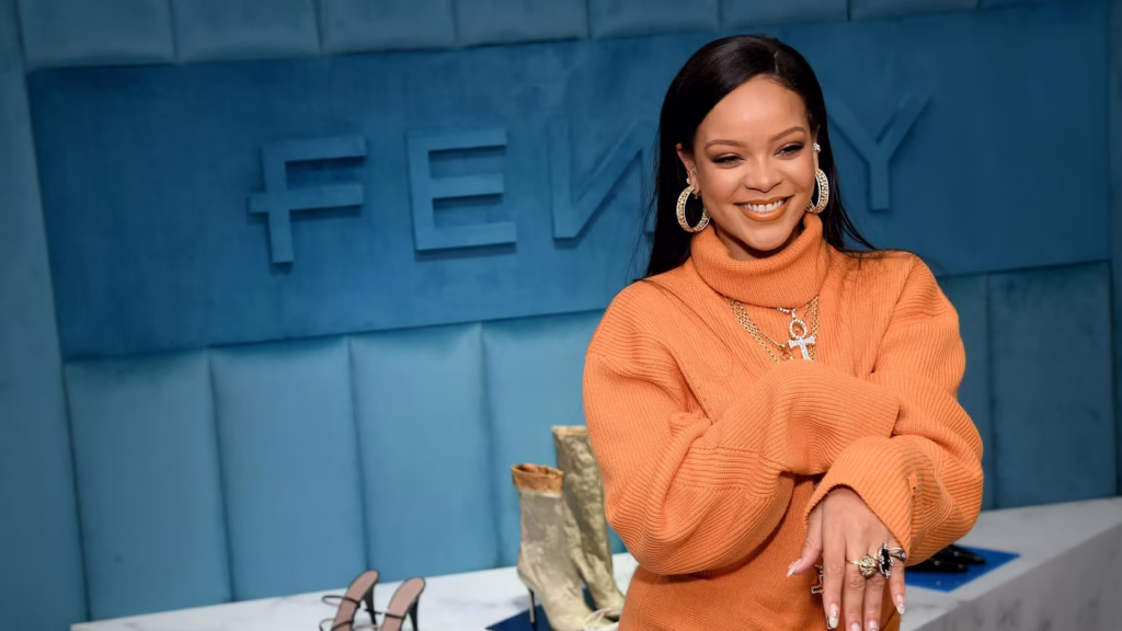 Rihanna smiling at Fenty Beauty event in orange sweater representing her $2.8 billion inclusive beauty empire