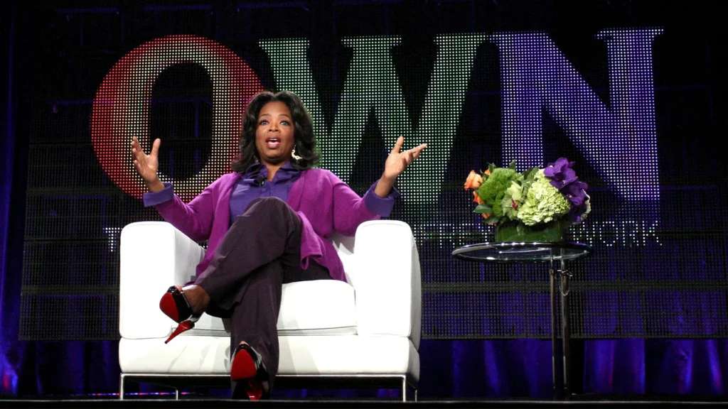 Oprah Winfrey at OWN Network event speaking on stage representing her cable television empire that generates over 75 million dollars annually after dramatic turnaround from near failure to profitable network owned jointly with Warner Bros Discovery