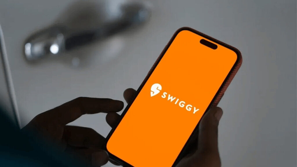 Swiggy delivery partner holding smartphone with orange Swiggy app logo showing dark store strategy for quick commerce profitability
