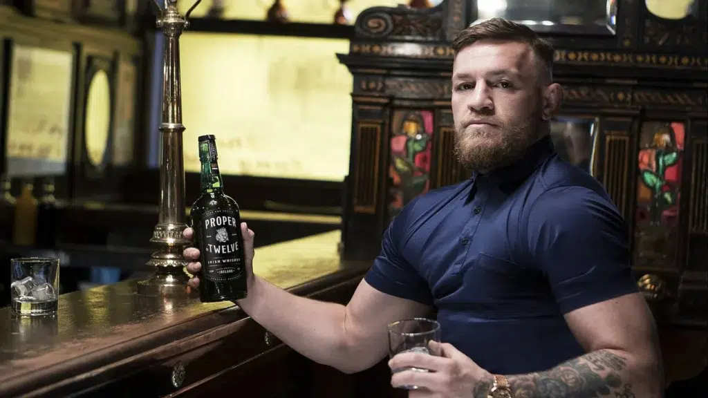Conor McGregor holding Proper No. Twelve Irish whiskey bottle showing the brand he sold for $600 million to Proximo Spirits