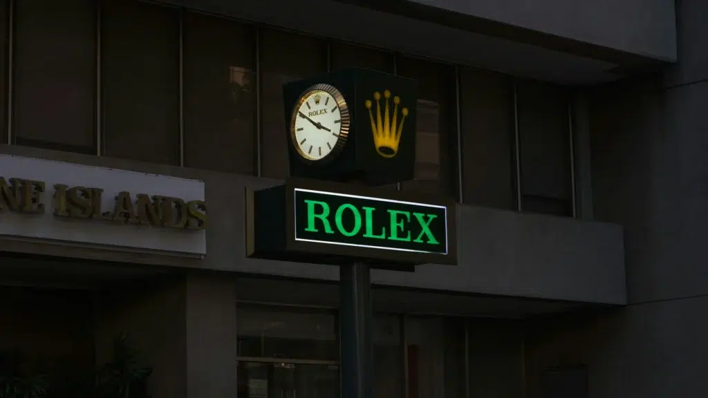 Rolex store sign illuminated at night showing crown logo demonstrating brand's controlled scarcity and luxury exclusivity strategy