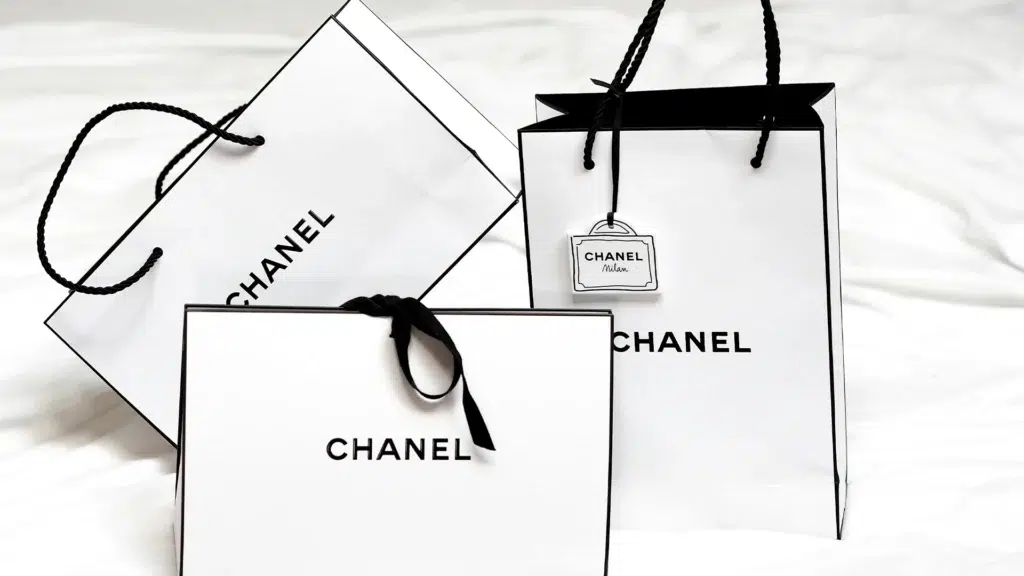 Chanel shopping bags and gift packaging in signature white with black trim showing luxury brand presentation that supports premium pricing and exclusivity perception