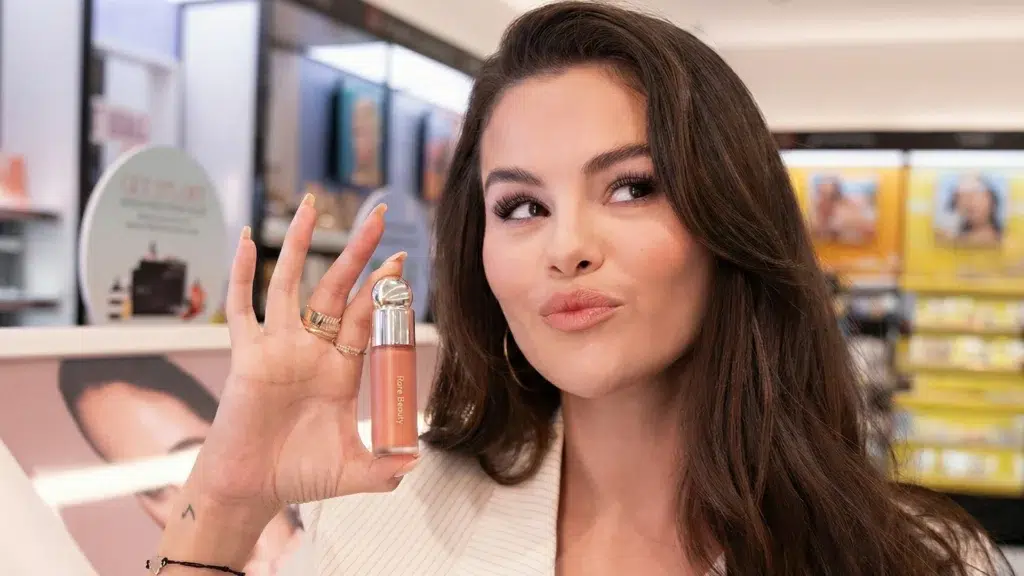 Selena Gomez holding Rare Beauty Soft Pinch Liquid Blush showing the $2.7 billion beauty brand that beats Kylie Cosmetics and Fenty