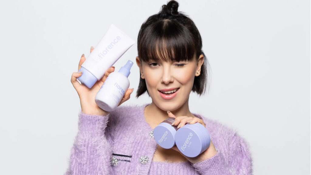 Millie Bobby Brown holding Florence by Mills skincare products showing the clean beauty brand she launched at 15 and owns majority stake in