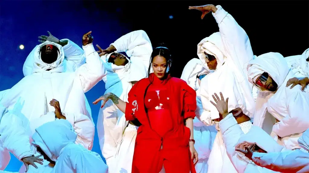 Rihanna in red Loewe jumpsuit performing at Super Bowl LVII halftime show surrounded by dancers in white revealing pregnancy