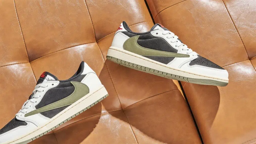 Travis Scott Air Jordan 1 Low sneakers in black white and olive green colorway with backwards swoosh on tan leather couch