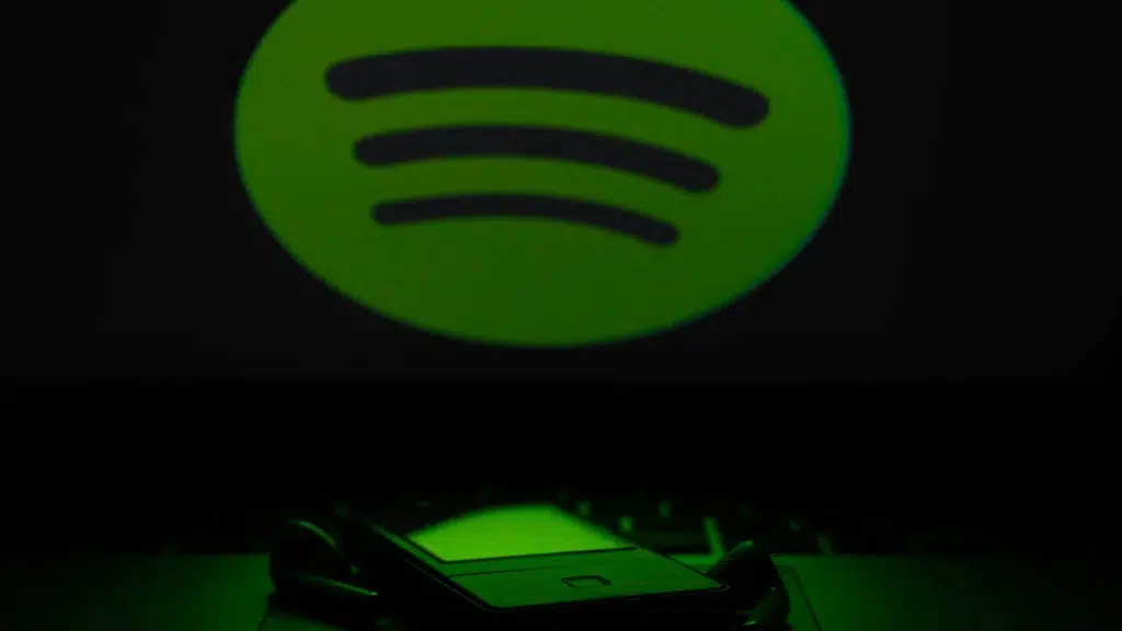 Spotify logo projected in green light on dark wall with phone and earphones below