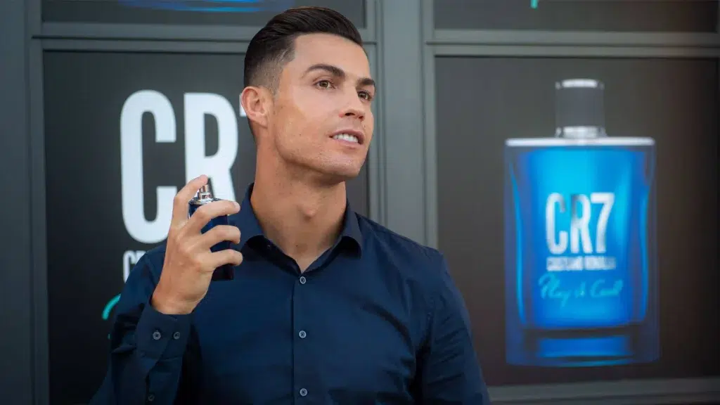 Cristiano Ronaldo holding a CR7 fragrance bottle at a brand event, representing his CR7 personal brand spanning fashion, fitness, hotels, and fragrance