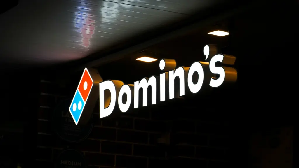 Domino's Pizza illuminated storefront sign at night on brick wall showing brand logo and delivery service